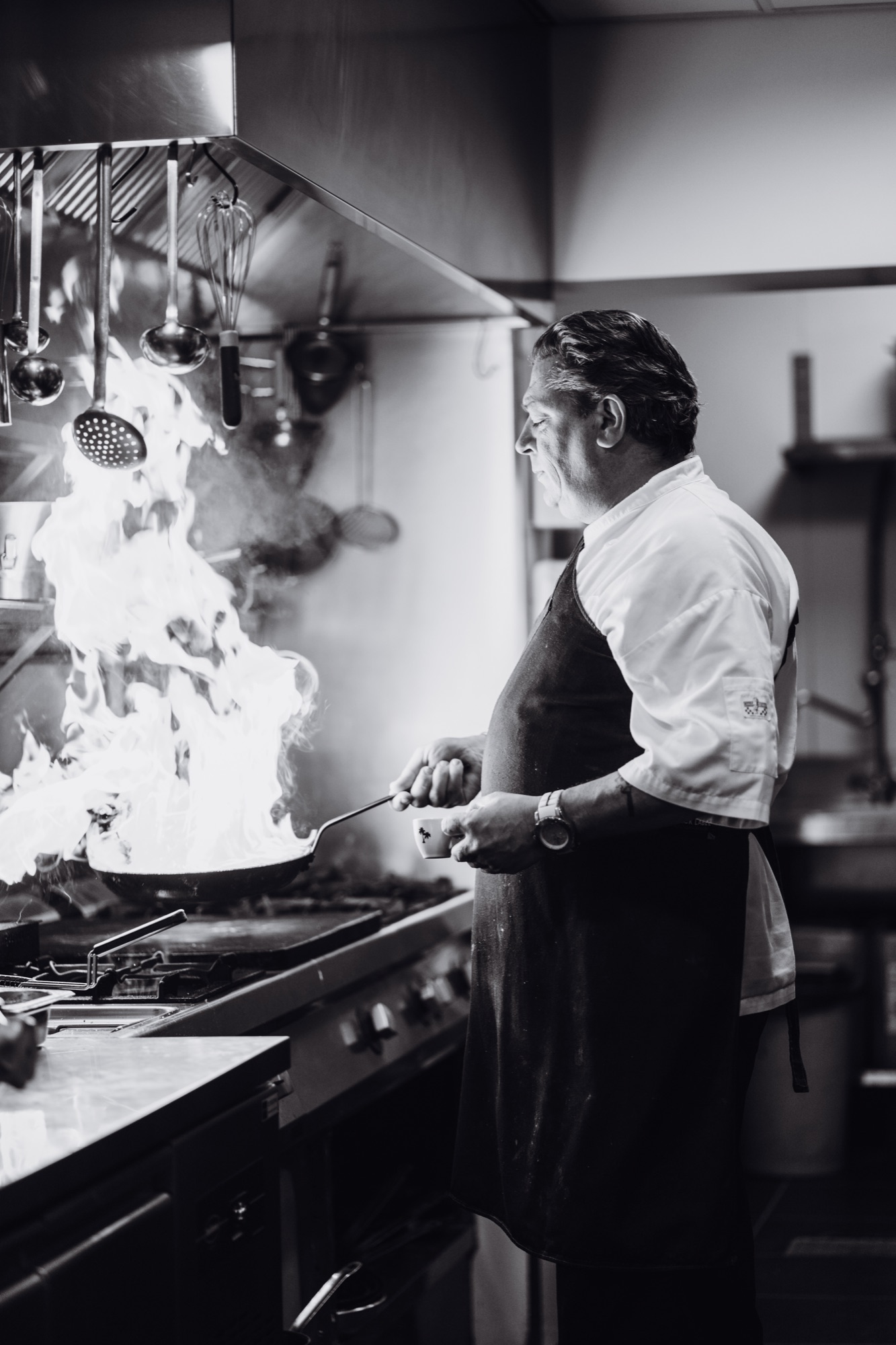 Chef flambeert een pan in de keuken, horecafotografie voor Koffielovers