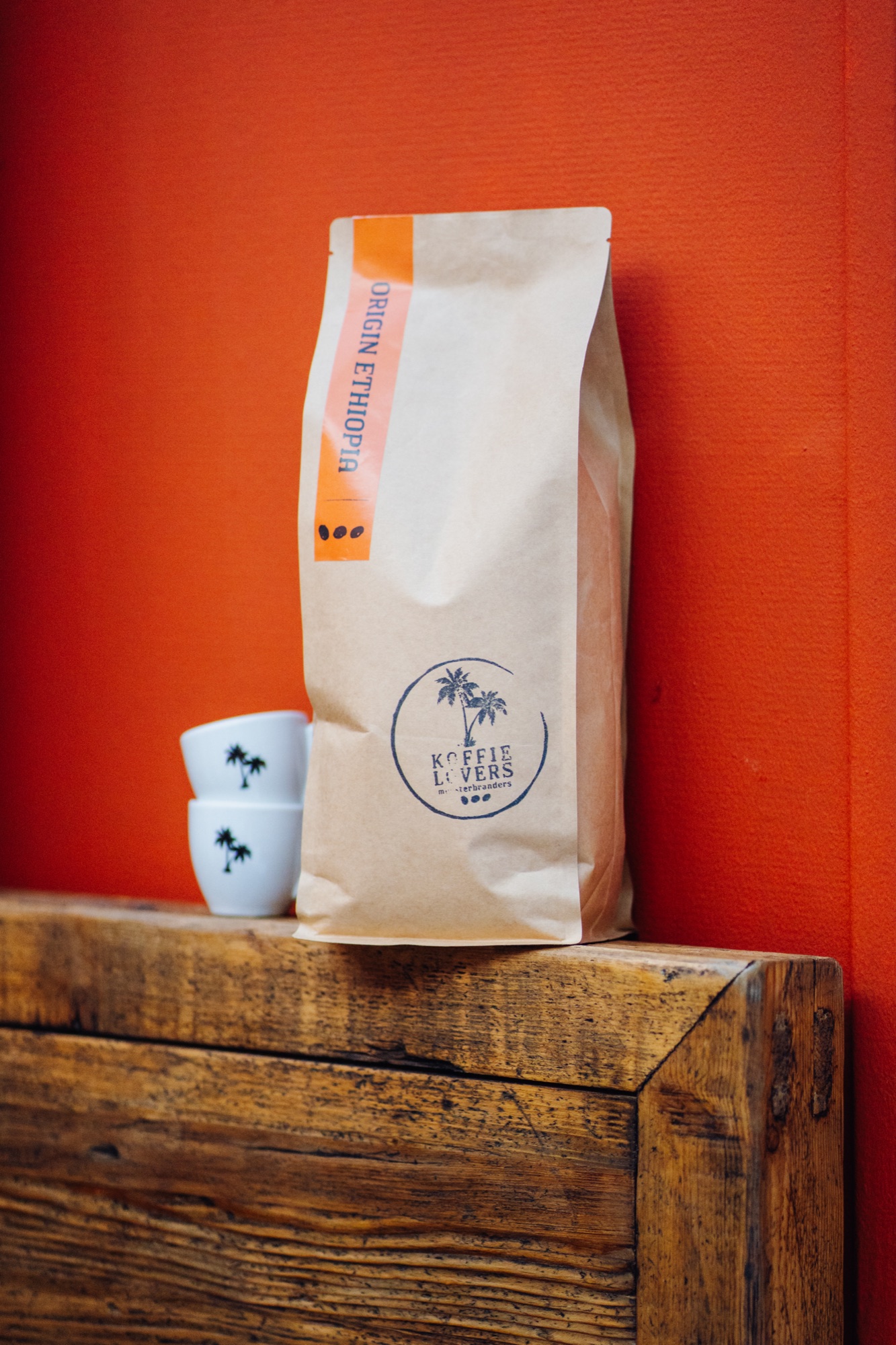 Koffielovers koffiezak en kopjes tegen een oranje wand